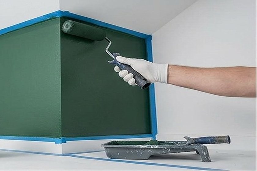 Maler rollt dunkelgrüne Wandfarbe auf eine abgeklebte Wand